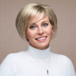 Image of a headshot of a woman wearing a white sweater. The woman is smiling with her head slightly tilted to the left.