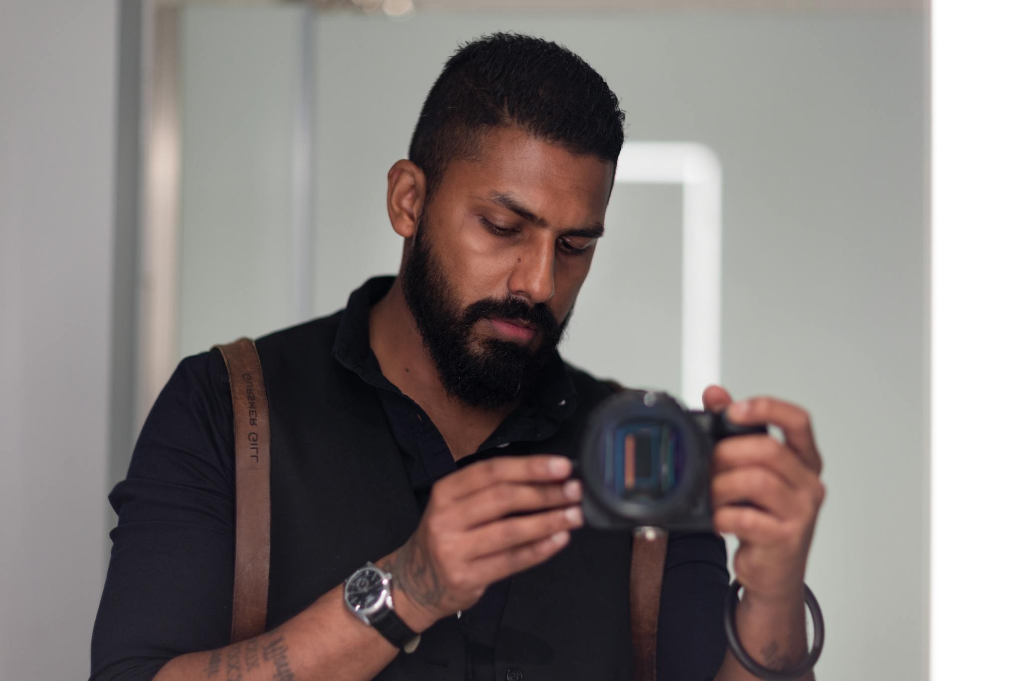 A bearded man concentrates on his camera in an indoor setting, showcasing focus and dedication.
