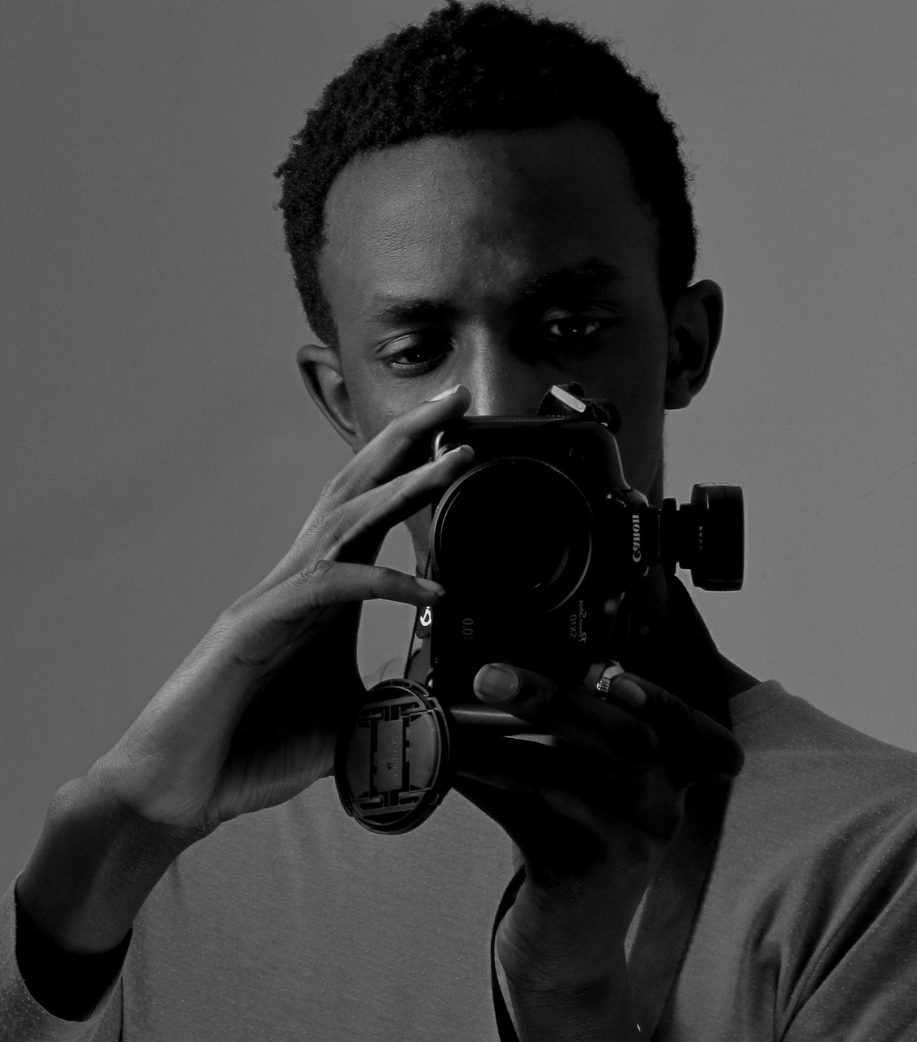 A black and white portrait of a man holding a DSLR camera, focused on capturing a photograph.