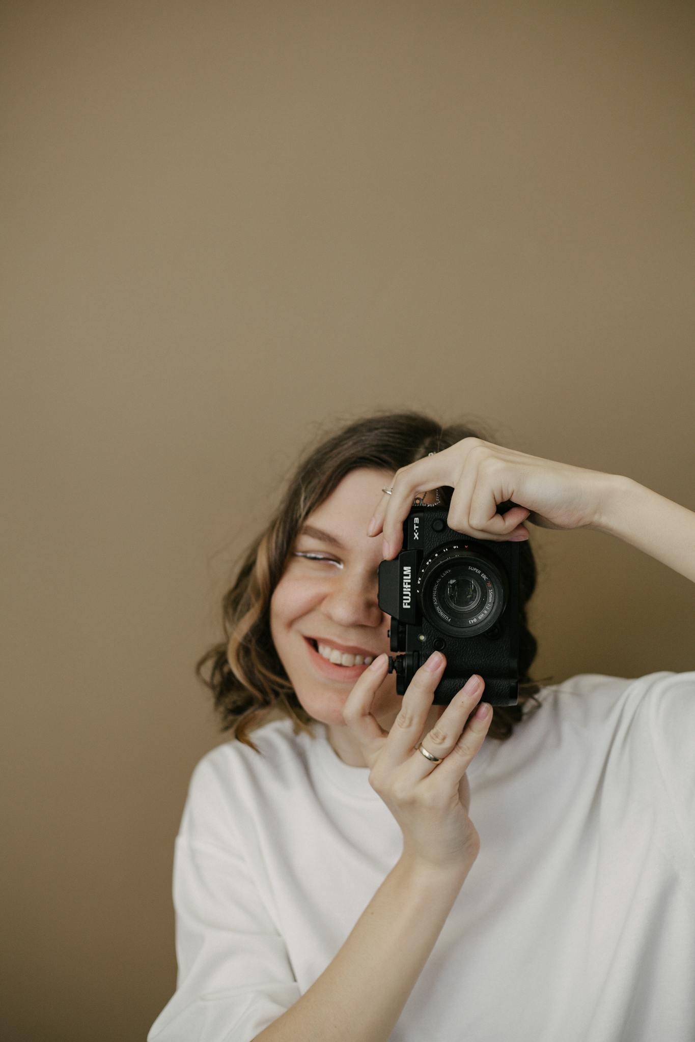 A smiling woman holding a camera against a neutral background.